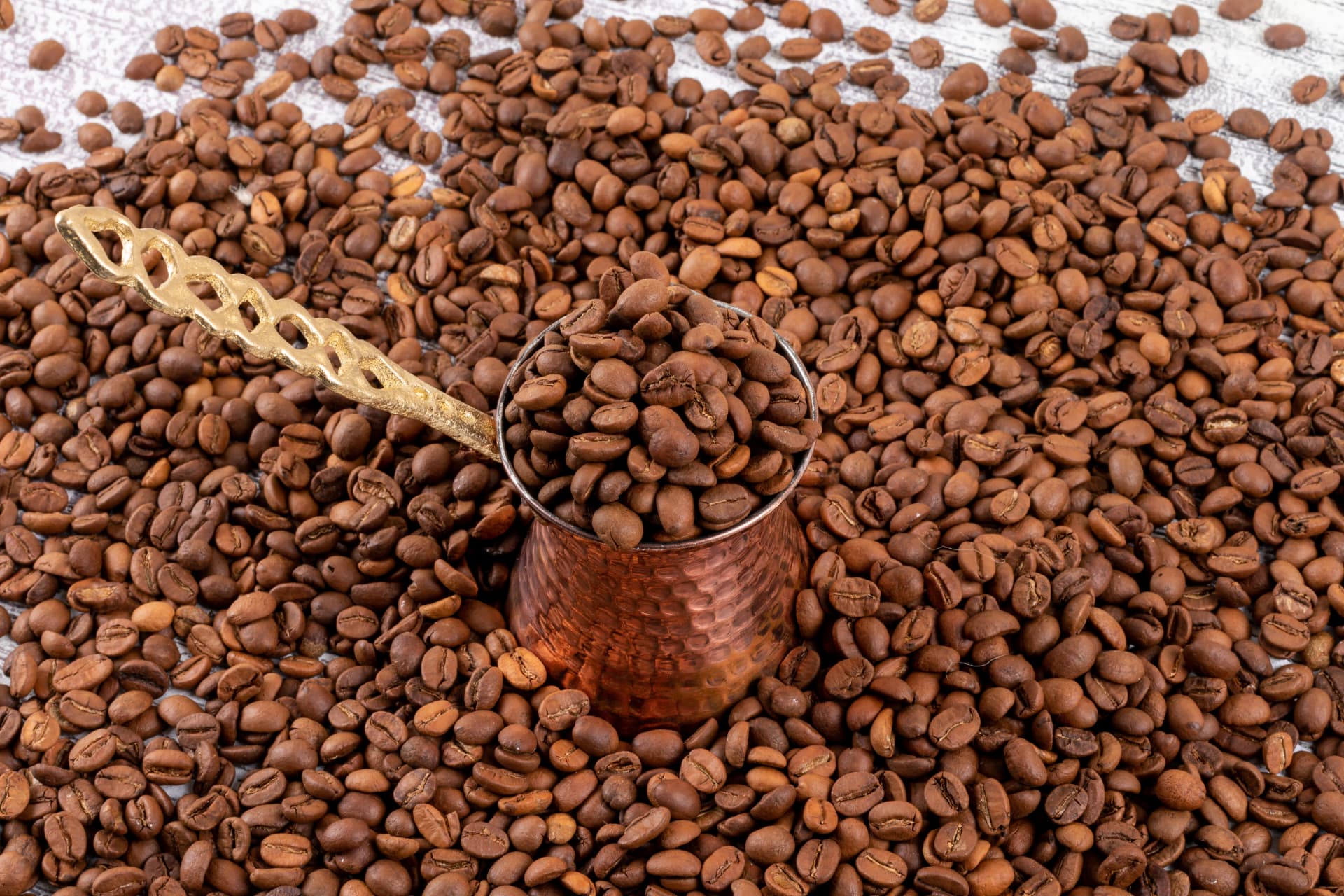 Roasted coffee beans filling a hammered copper pot with a golden scoop